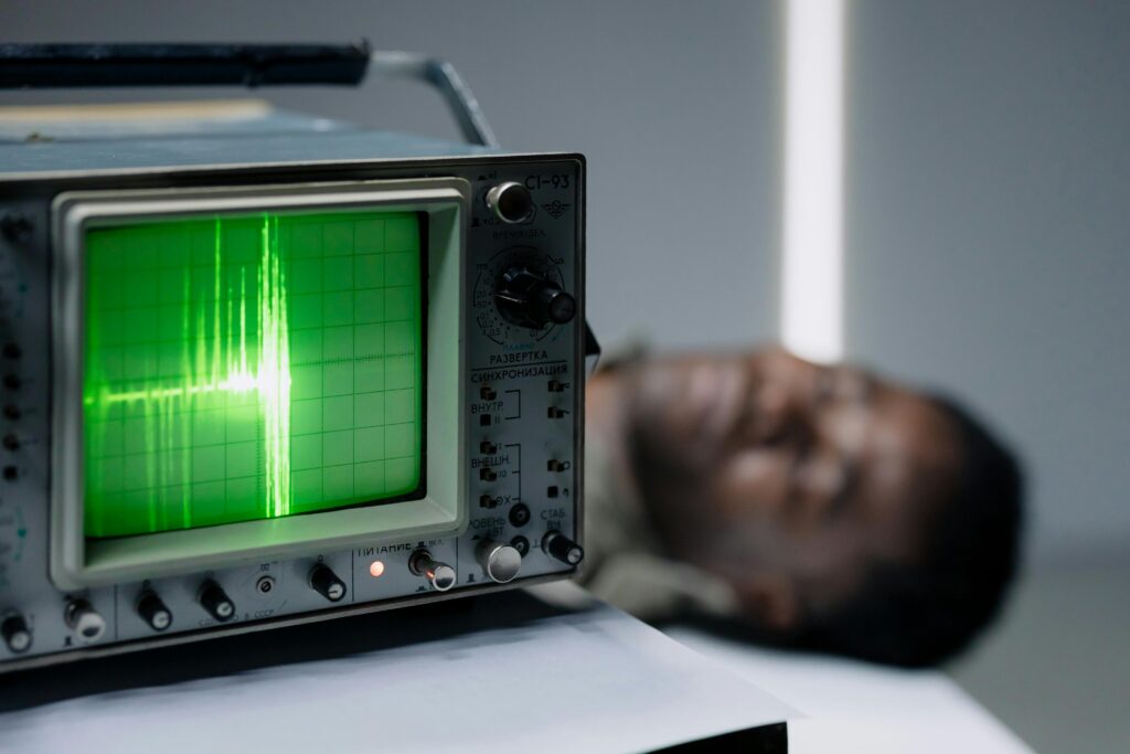 Close-up of a vintage oscilloscope displaying a green waveform next to a blurred person.